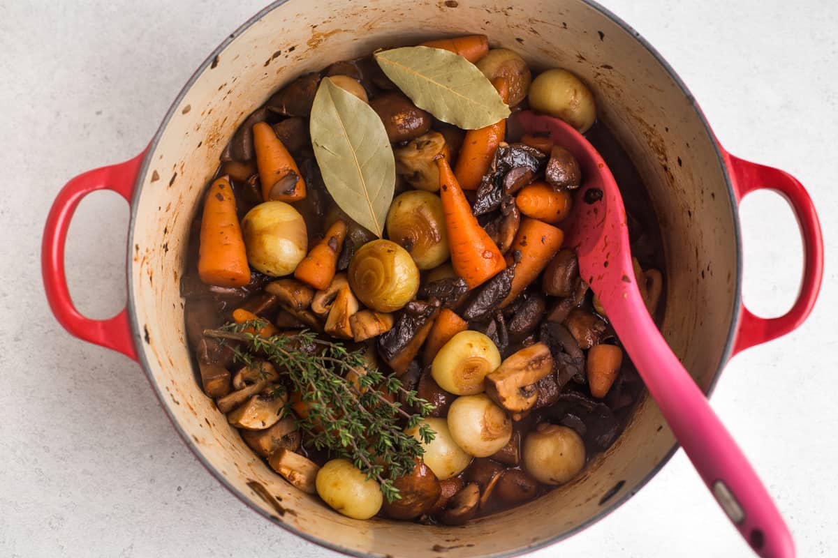 Onions, carrots and mushrooms in a large casserole dish with bay leaves and fresh thyme.