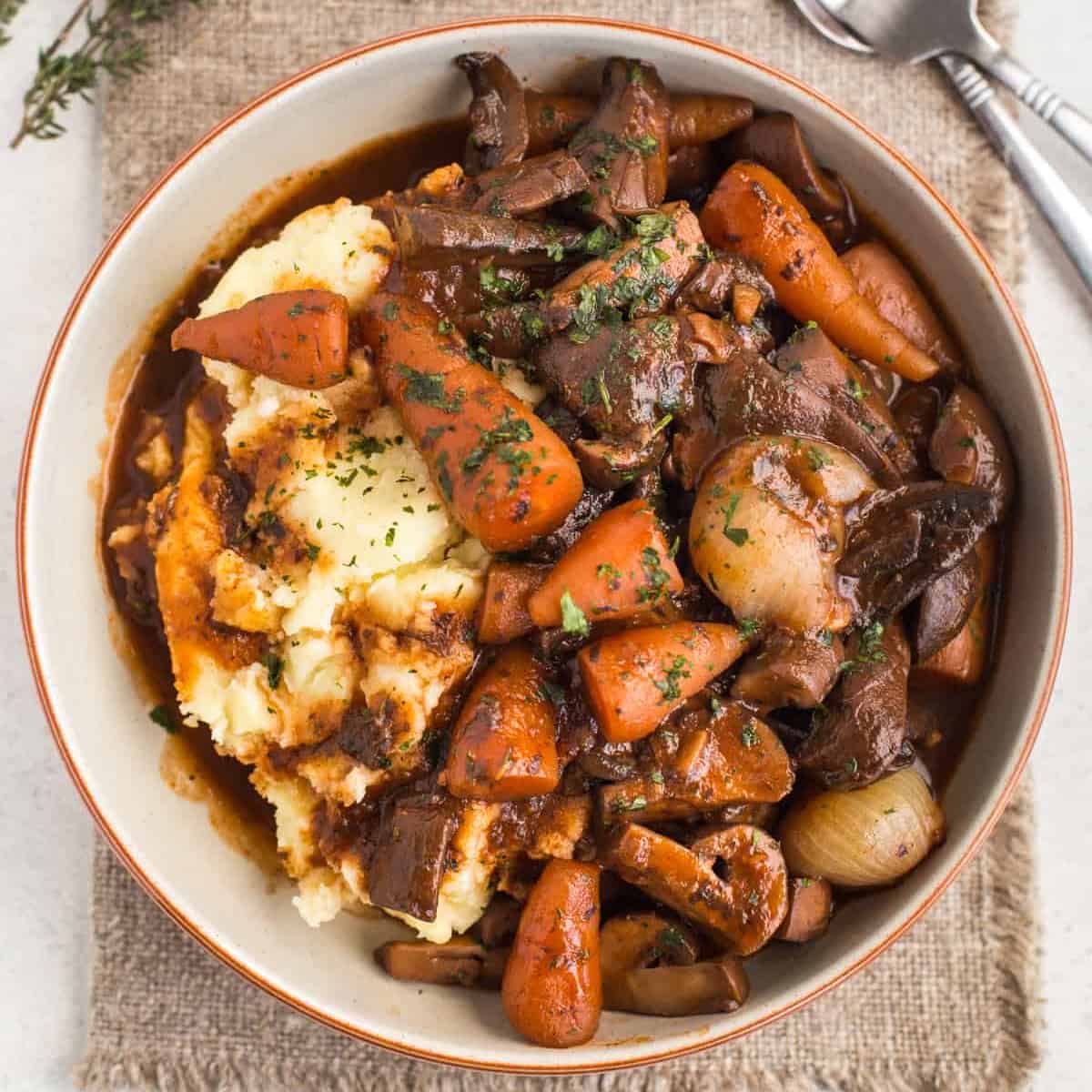 A bowlful of rich mushroom bourguignon stew served over mashed potato.