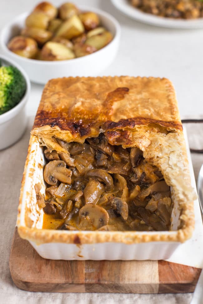 Mushroom stroganoff pie, served on a wooden board, with a scoop removed