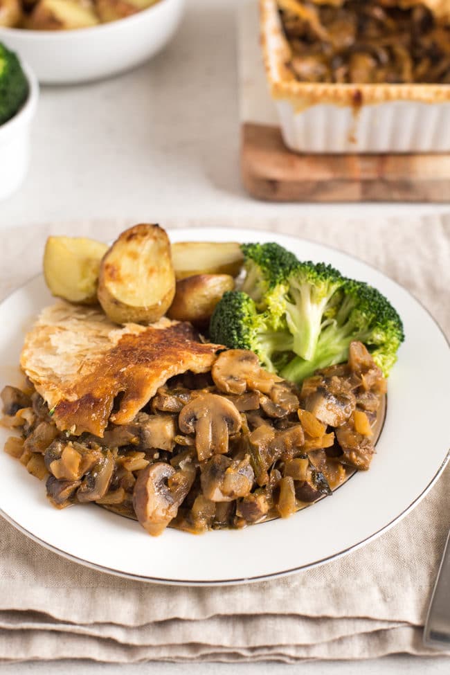 A portion of mushroom stroganoff pie on a plate, served with roast potatoes and broccoli