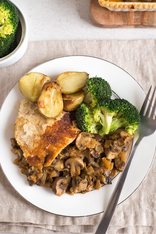 A portion of mushroom stroganoff pie on a plate, shot from above, served with roast potatoes and broccoli