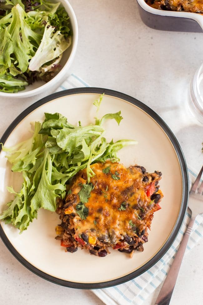 A portion of cheesy vegetarian chilli and rice bake on a plate with salad, shot from above
