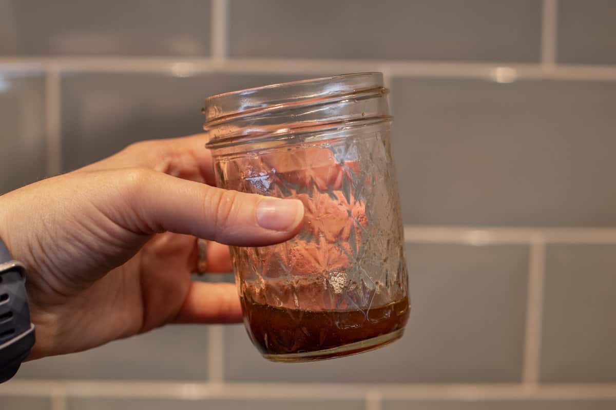 A hand holding a small jar with balsamic dressing.
