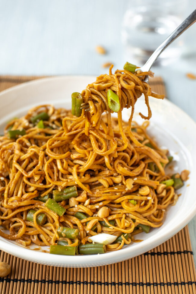 Peanut noodles being scooped by a fork.