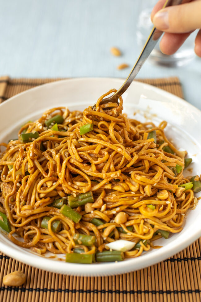 A bowl of peanut and sesame noodles being twirled with a fork.