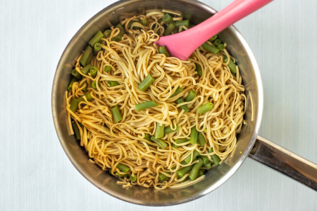 Noodles and green beans in a saucepan.