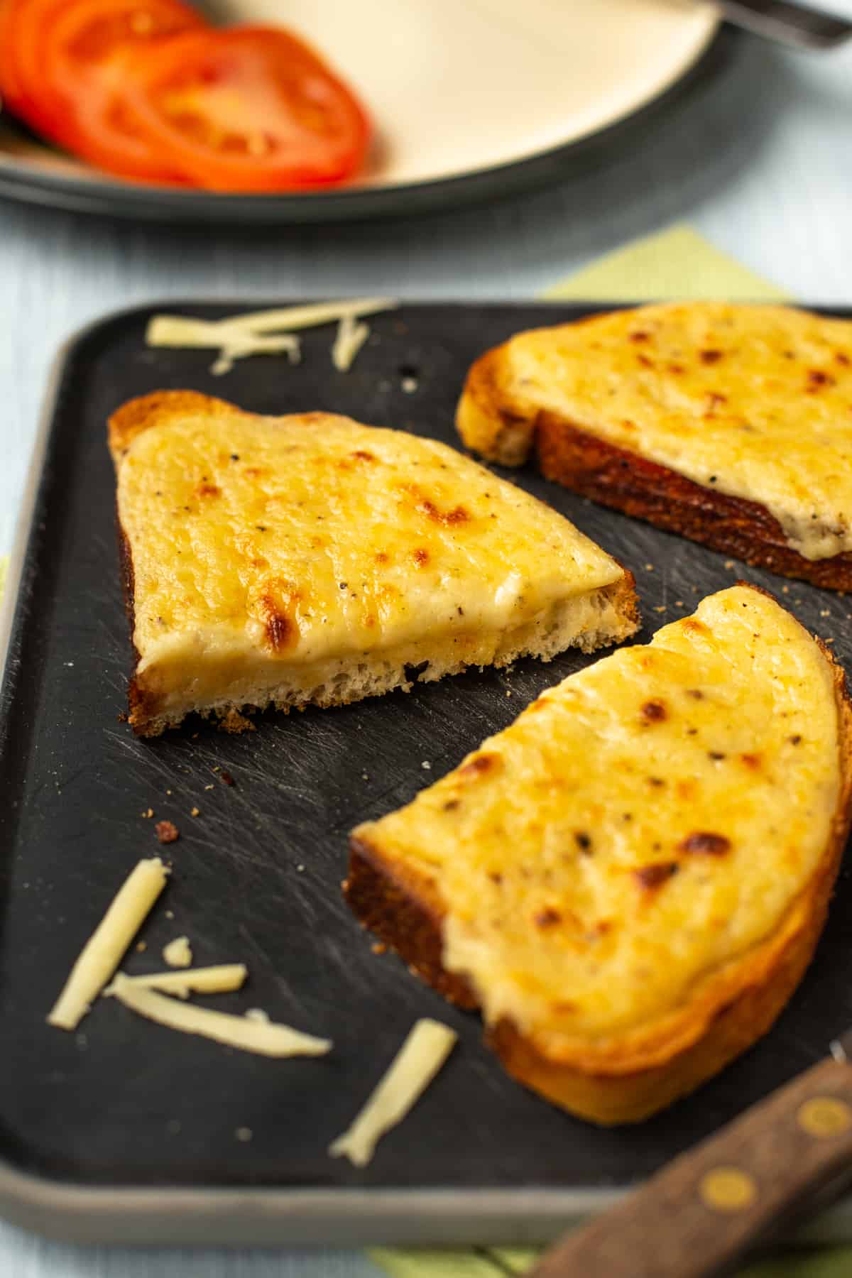 A slice of Welsh rarebit cut in half on a chopping board.