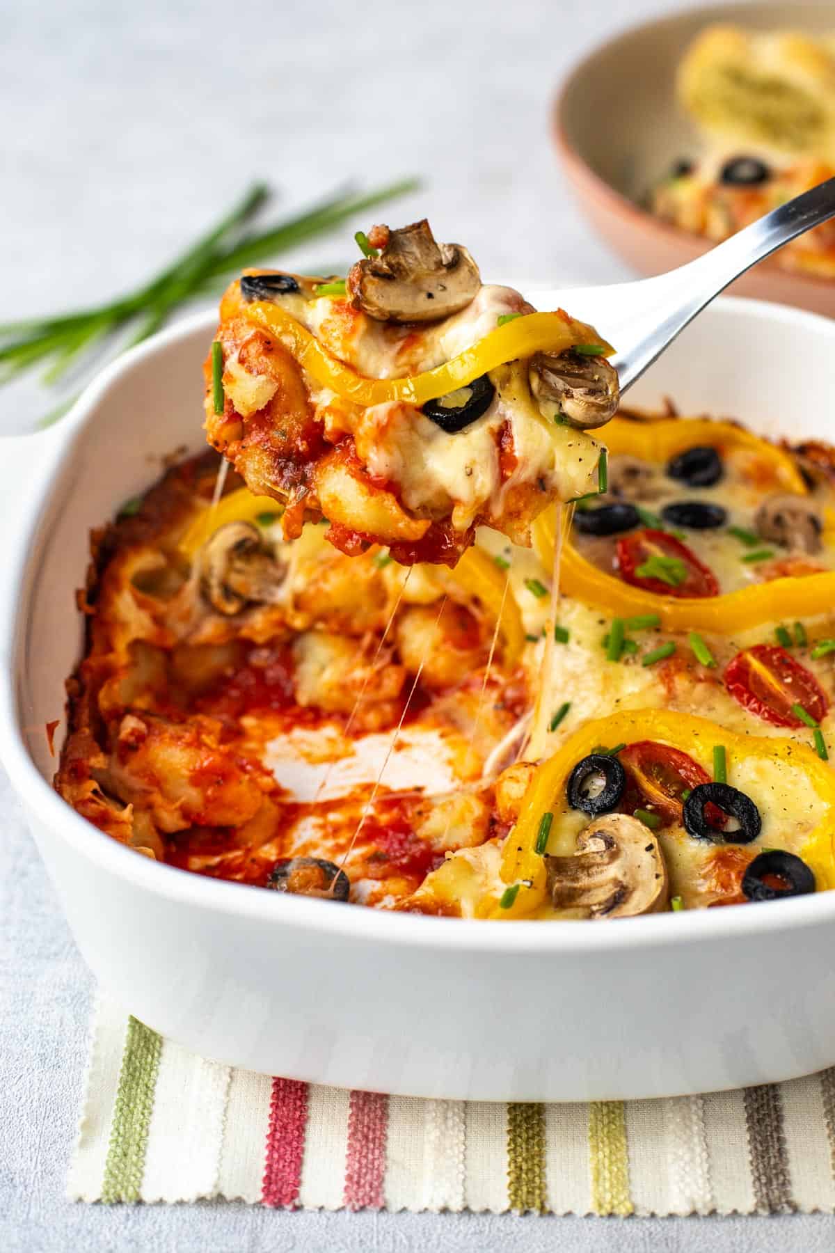 A large spoon scooping some cheesy pizza baked gnocchi.
