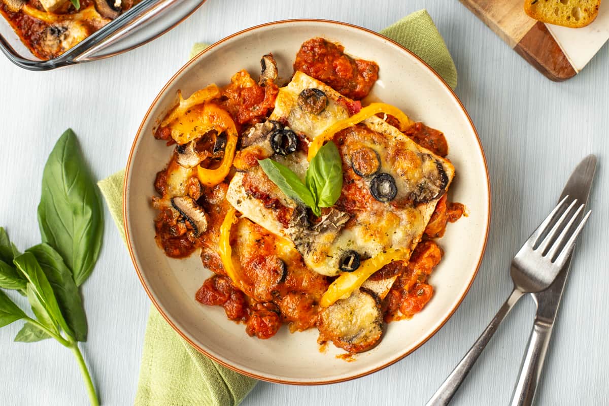 A piece of tofu in tomato sauce, served in a bowl topped with fresh basil.