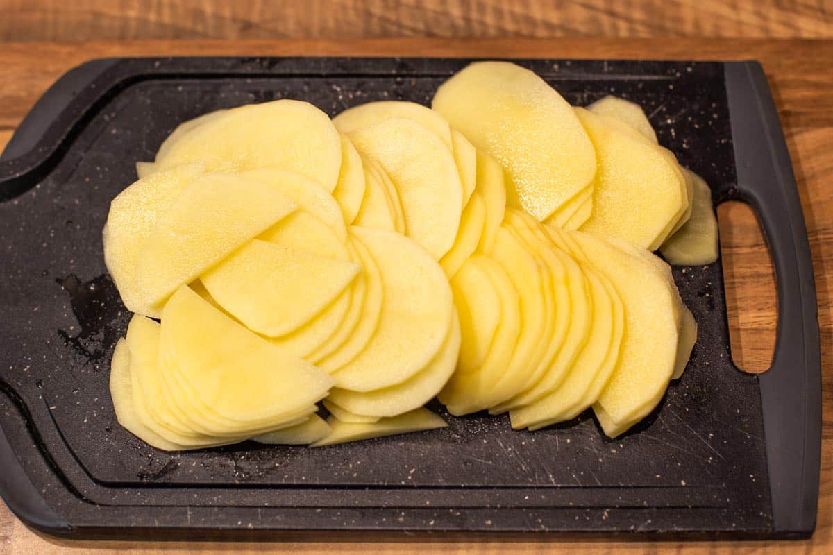 Thinly slices potatoes on a chopping board.