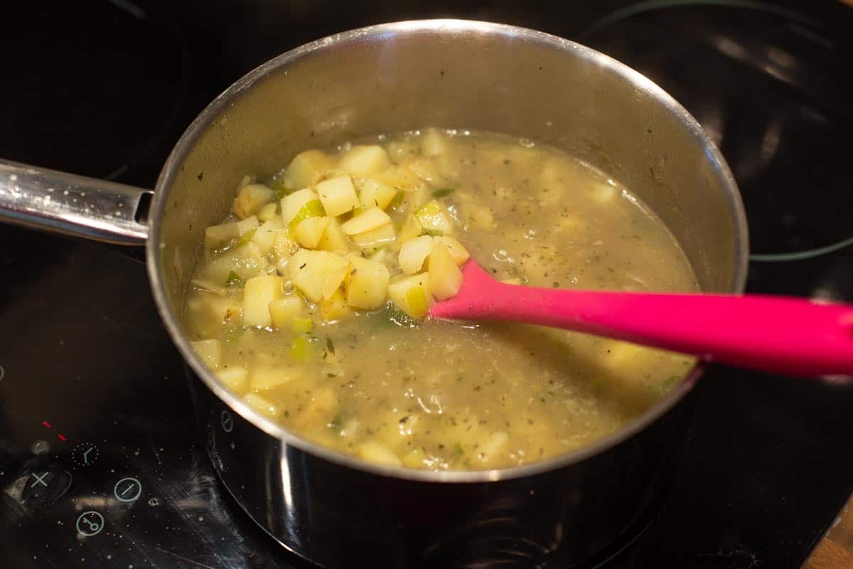Cooked potatoes and onions in stock in a saucepan.