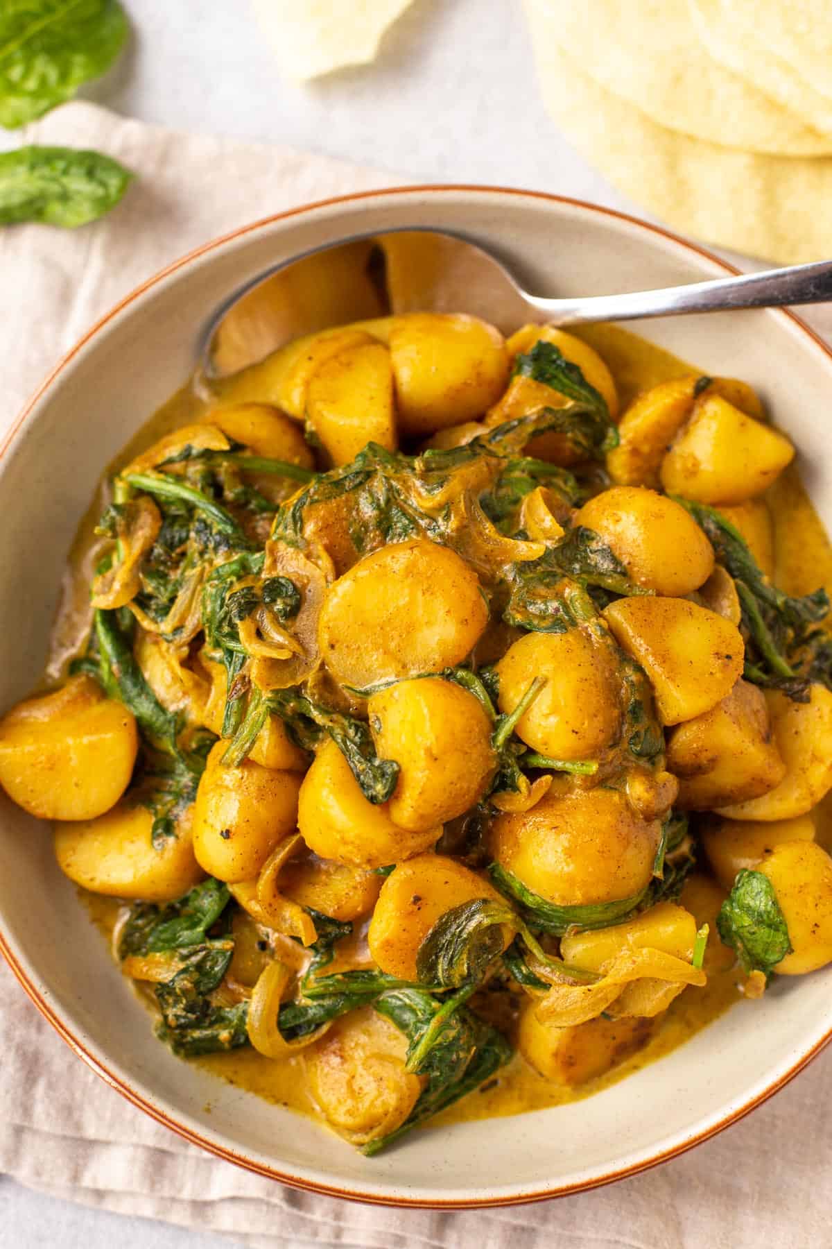 Creamy spinach and potato curry in a bowl with a spoon.