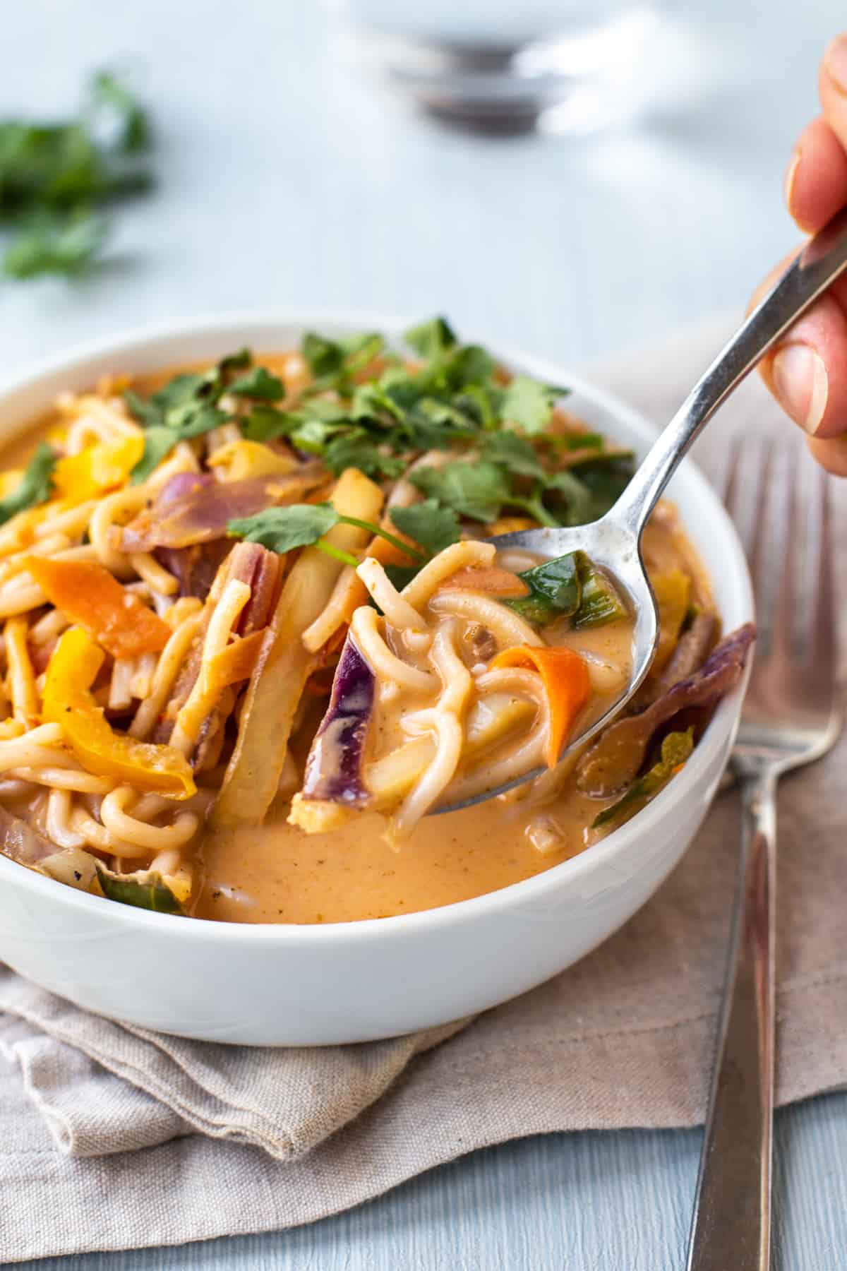 A spoon taking a scoop of Thai curry noodle soup.