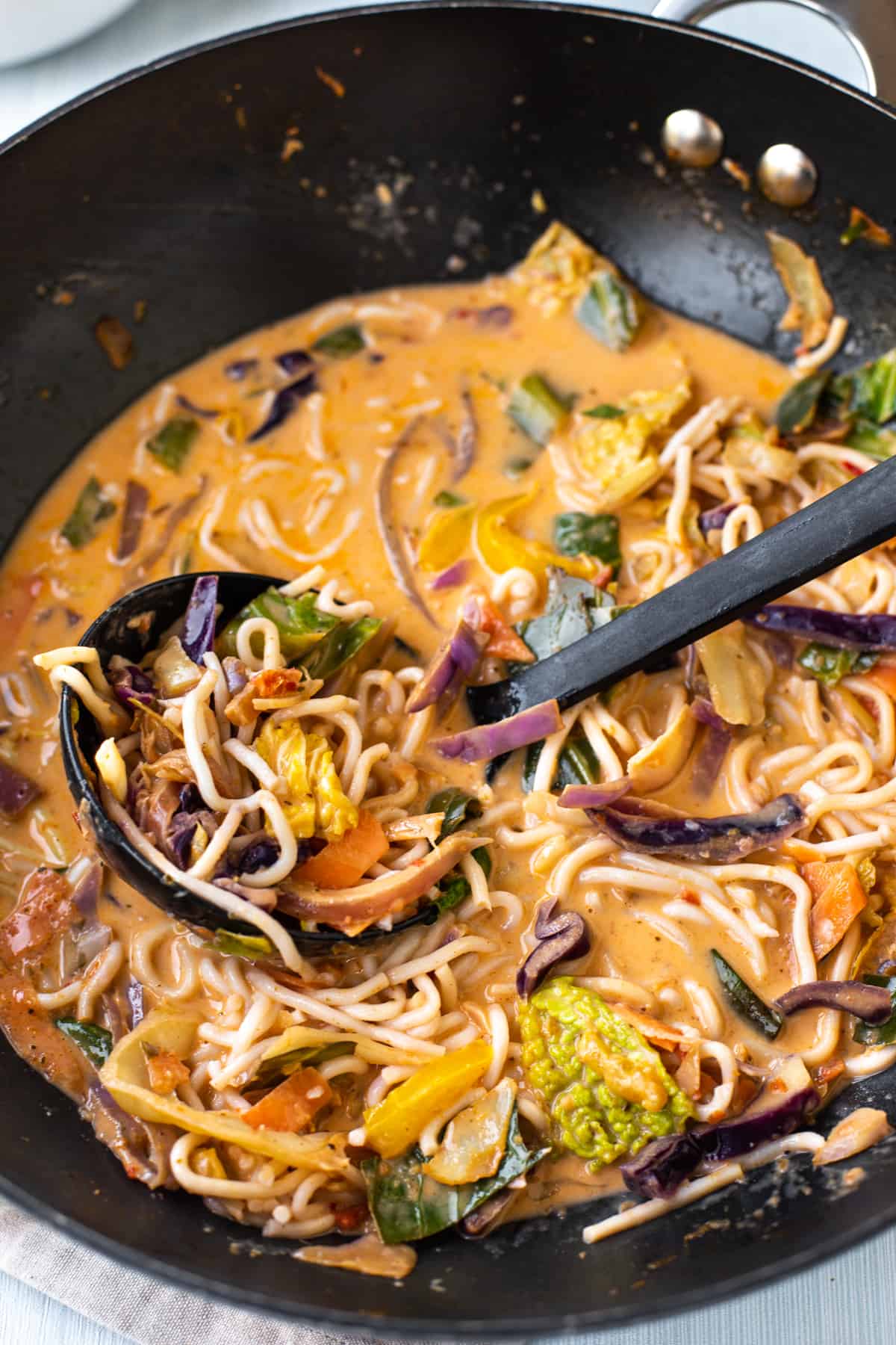 Thai curry noodle soup in a wok with a ladle.