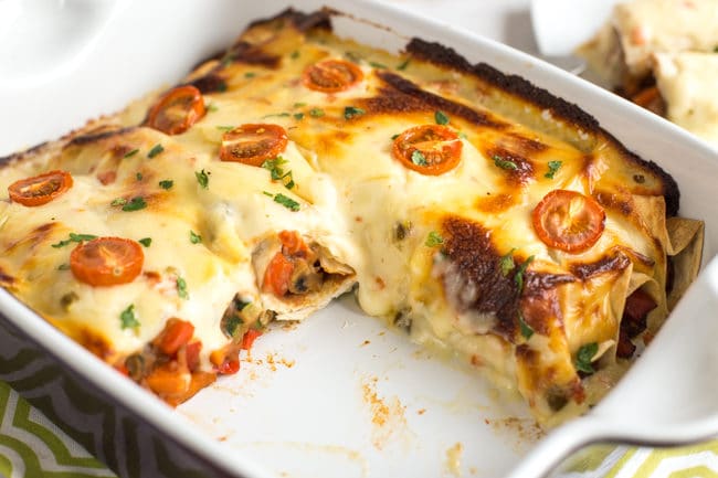 Refried bean enchiladas with jalapeno cheese sauce in a baking dish with a piece removed