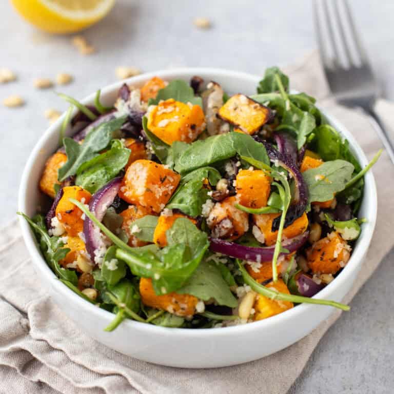 A portion of roasted butternut squash salad in a bowl with red onion and arugula.