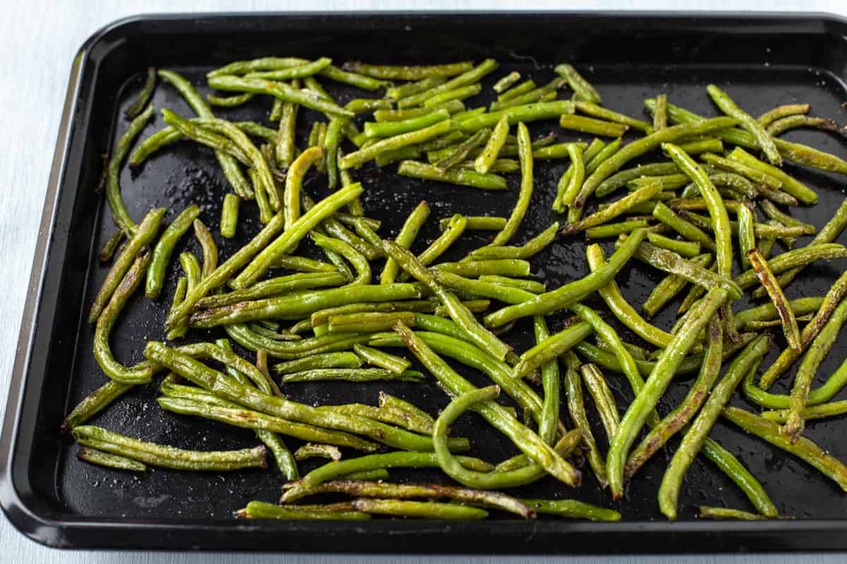 Roasted frozen green beans spread out on a baking tray.