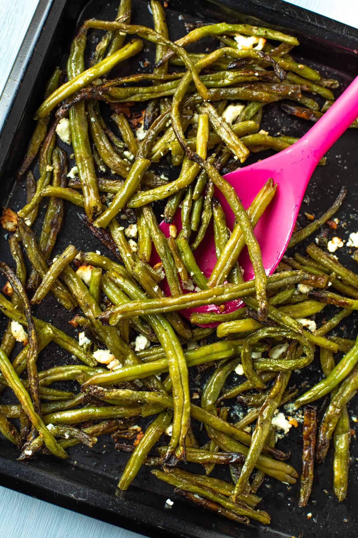 Roasted green beans with feta and lemon juice on a baking tray.