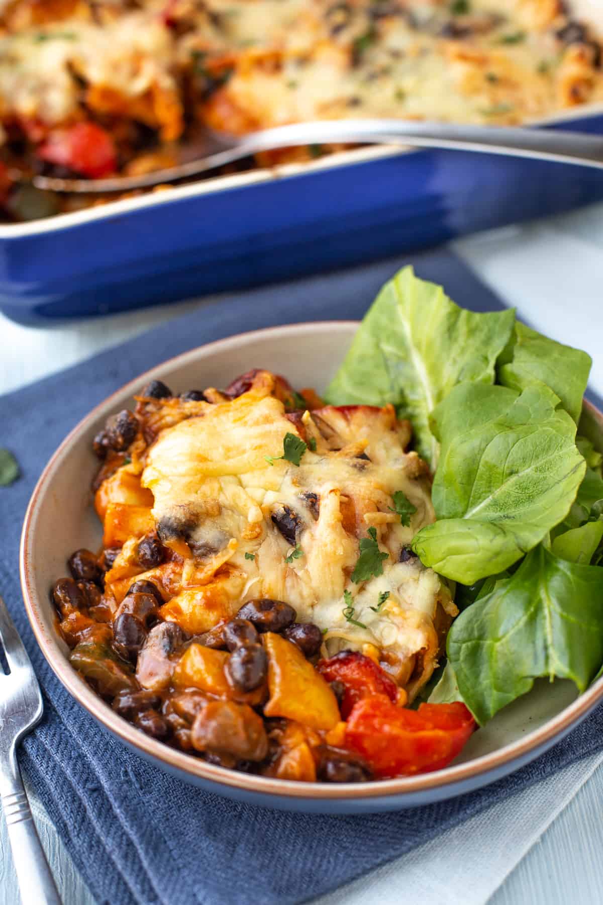 A portion of vegetarian enchilada casserole in a bowl with lettuce leaves.