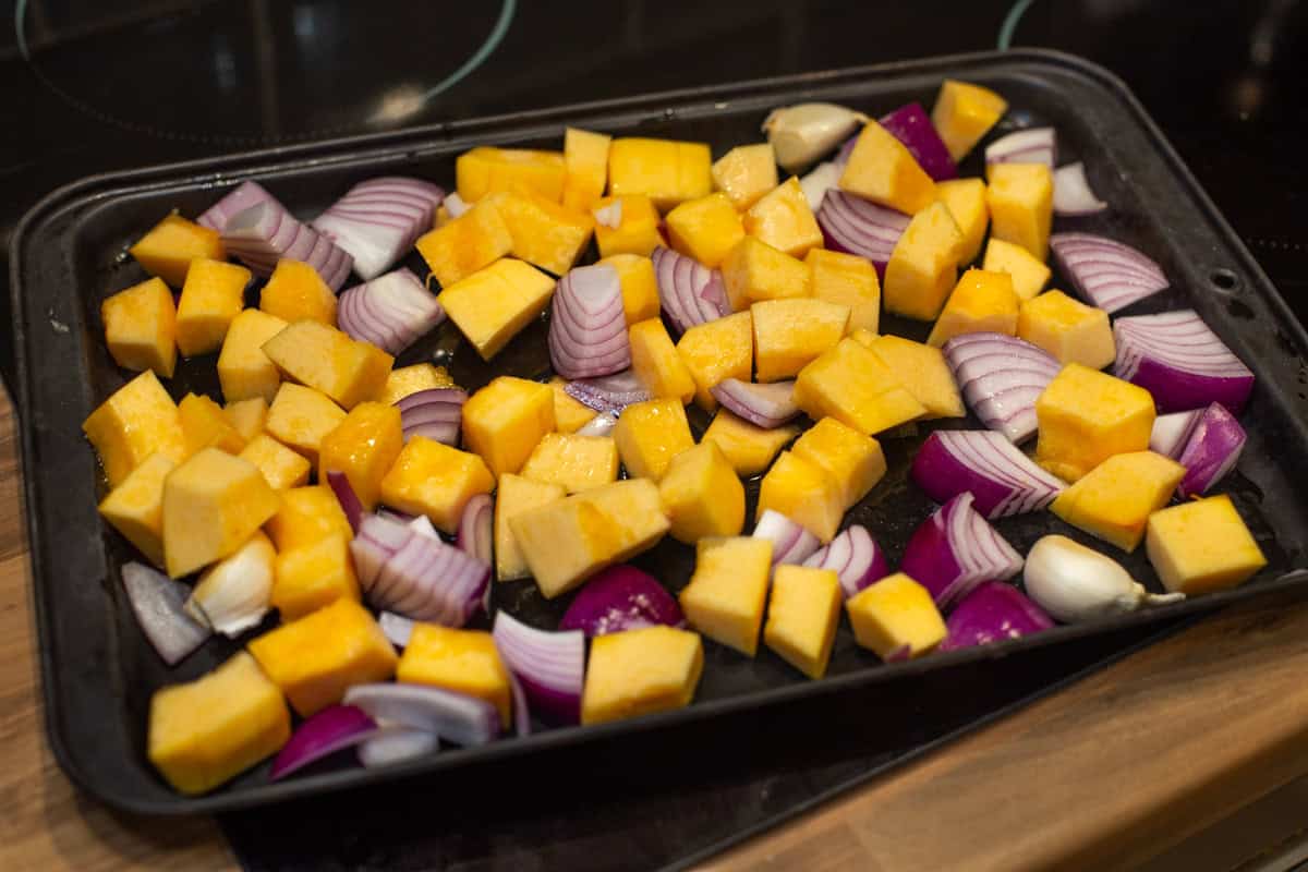 Raw pieces of pumpkin and red onion on a baking tray.
