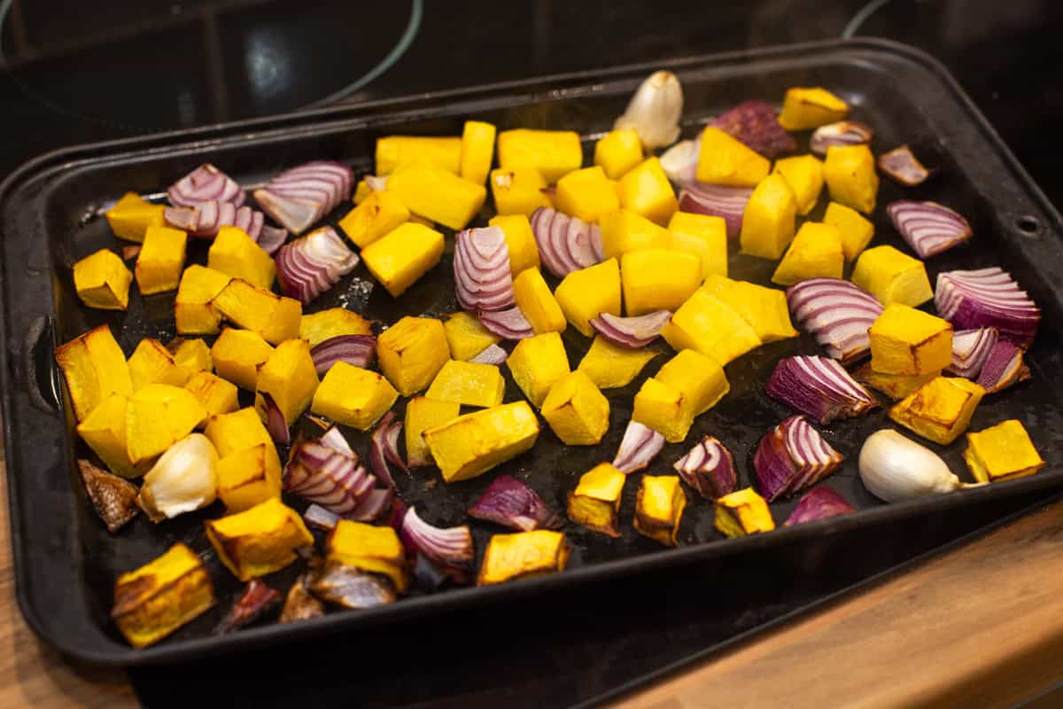 Roasted pumpkin and red onion on a baking tray.