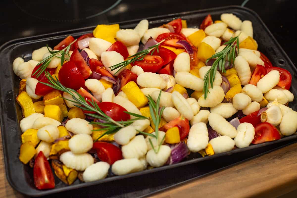 Uncooked gnocchi on a baking tray with tomatoes and rosemary.