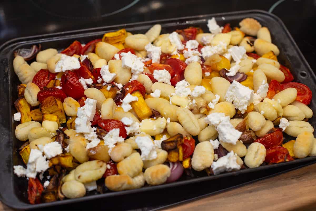 Roasted gnocchi and pumpkin on a baking tray topped with feta cheese.