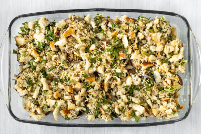 A dish of uncooked stuffed mushrooms with a herby breadcrumb topping.