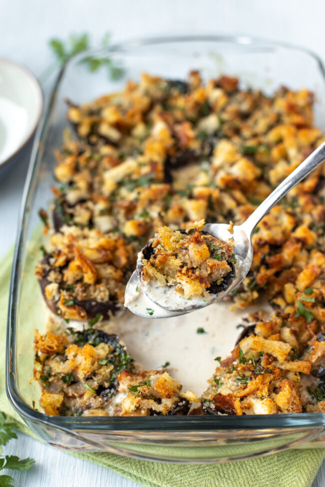 A spoon lifting a crispy stuffed mushroom from a baking dish.