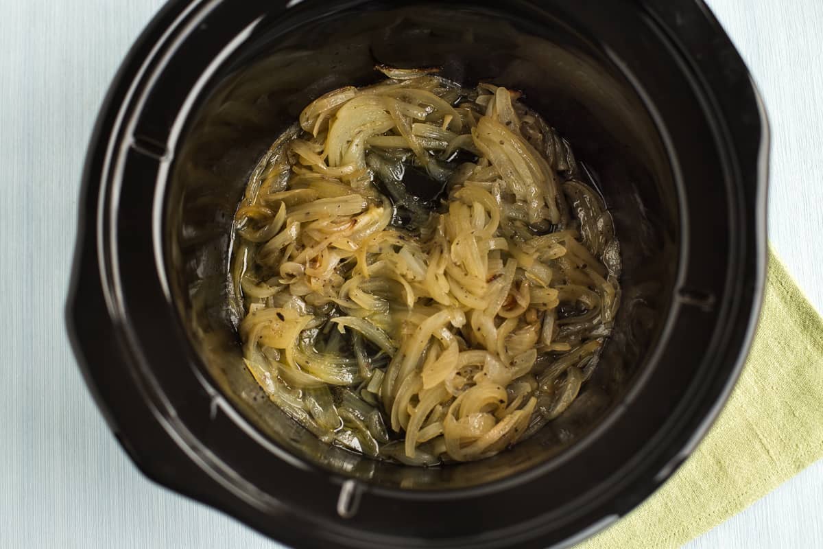 Lightly caramelised onions partway through cooking, in a slow cooker pot.