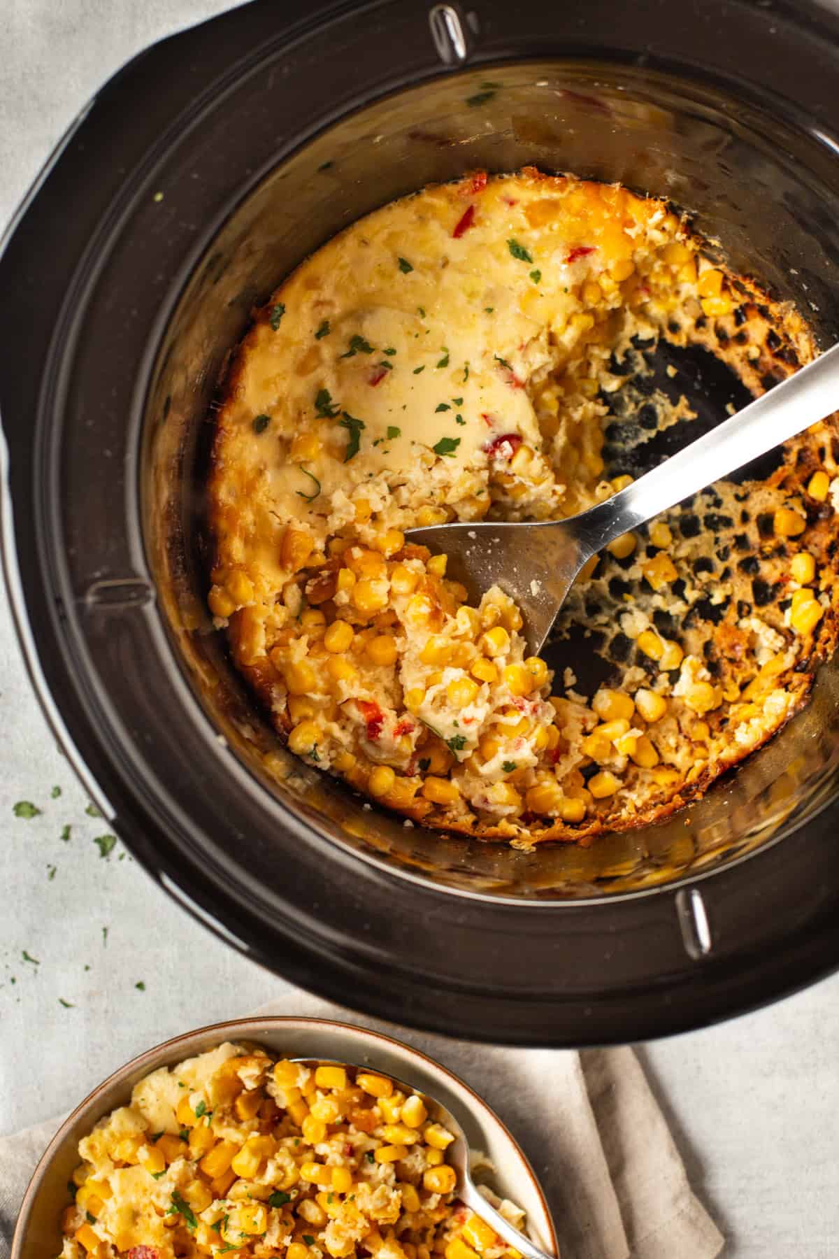 A large spoon taking a scoop of corn casserole from a slow cooker.