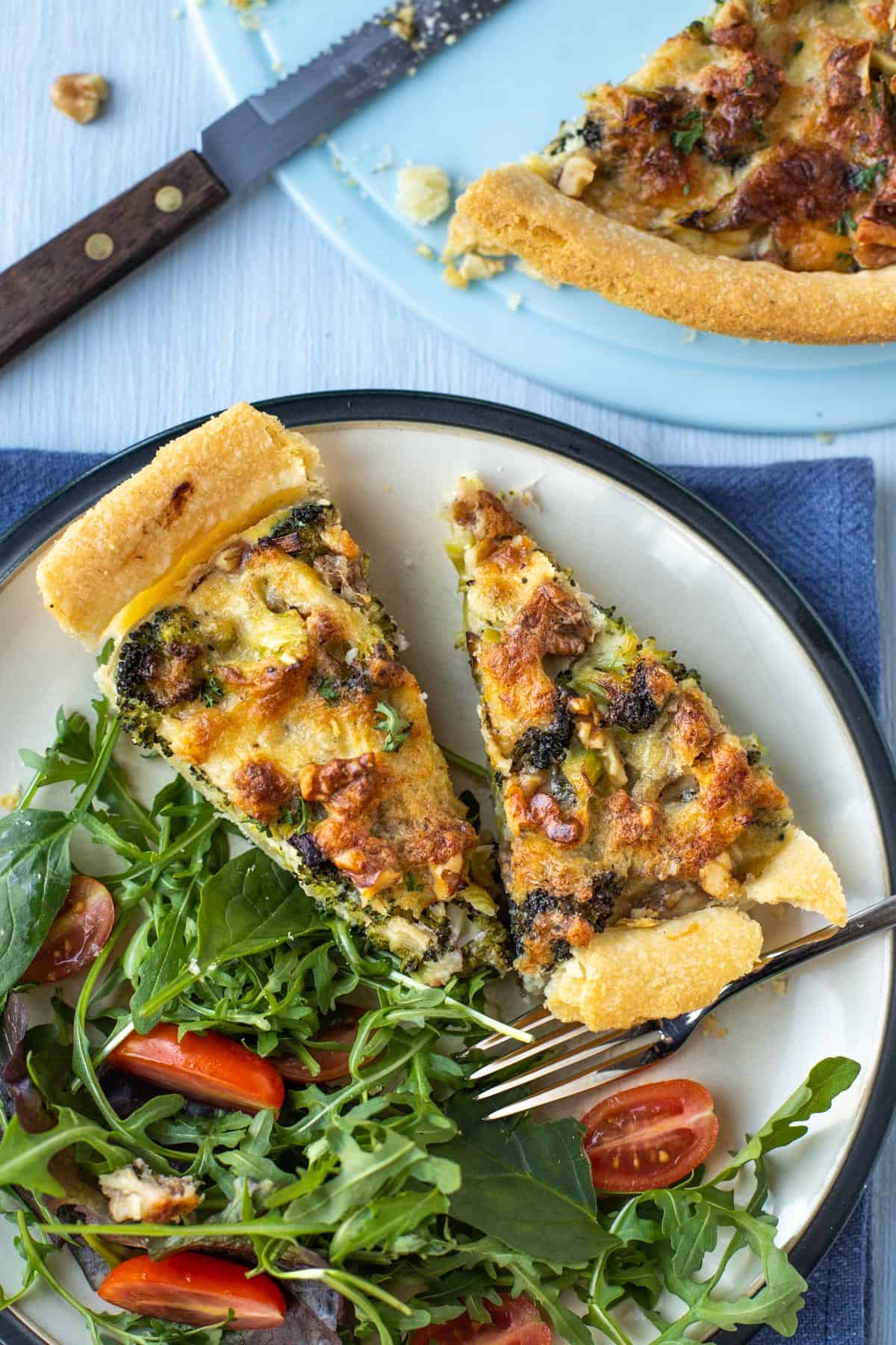Overhead shot of two slices of cheese and broccoli tart on a plate with salad.