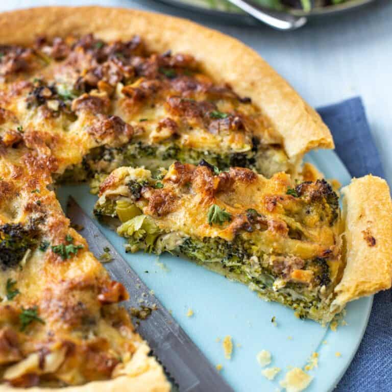 A slice of smoked cheese and broccoli tart being cut on a board.