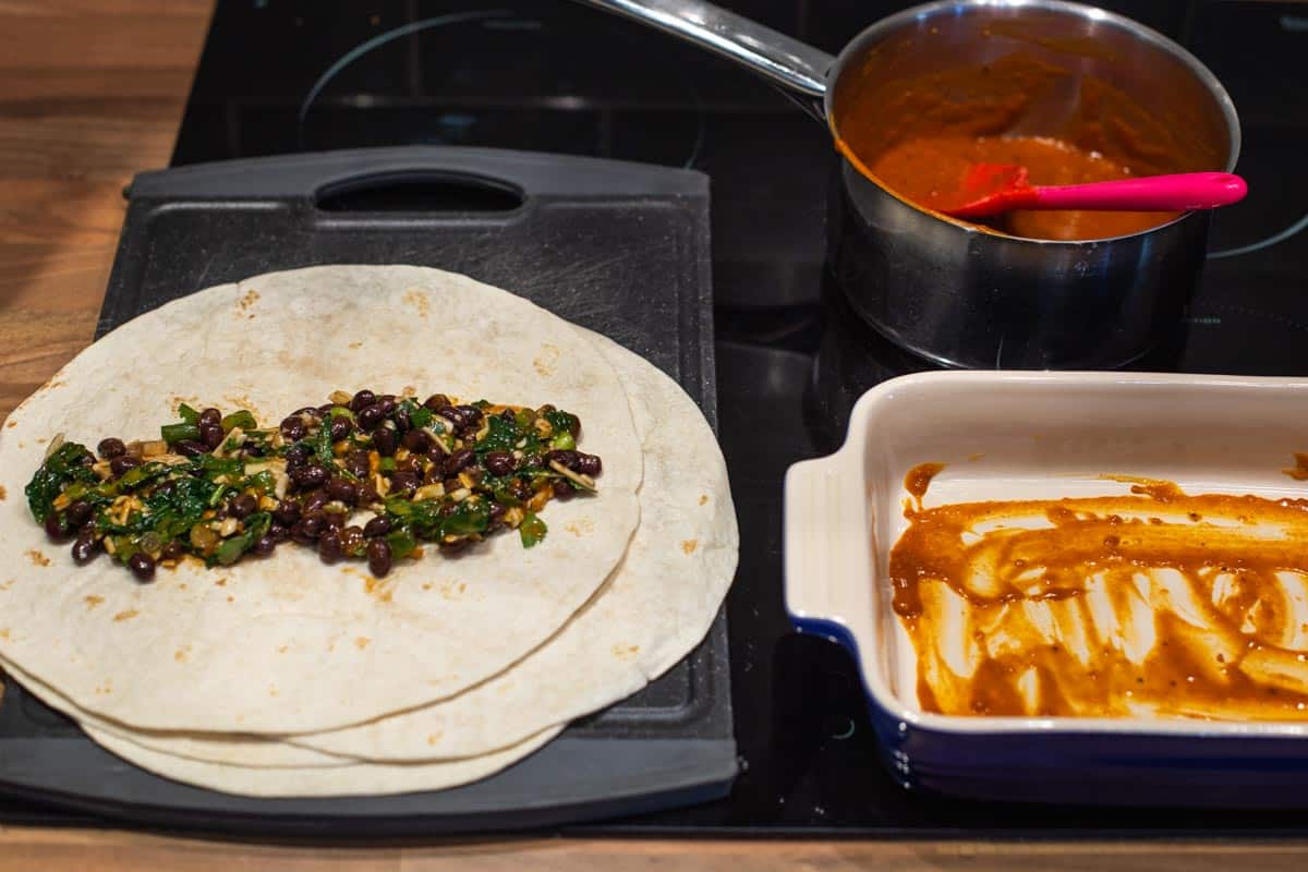 Vegetarian black bean enchiladas being filled on a chopping board.