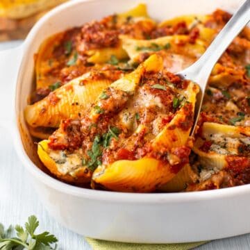 A spoon scooping a spinach and ricotta stuffed shell in tomato sauce from a baking dish.