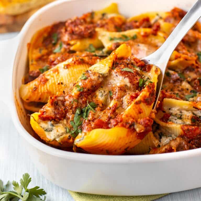 A spoon scooping a spinach and ricotta stuffed shell in tomato sauce from a baking dish.