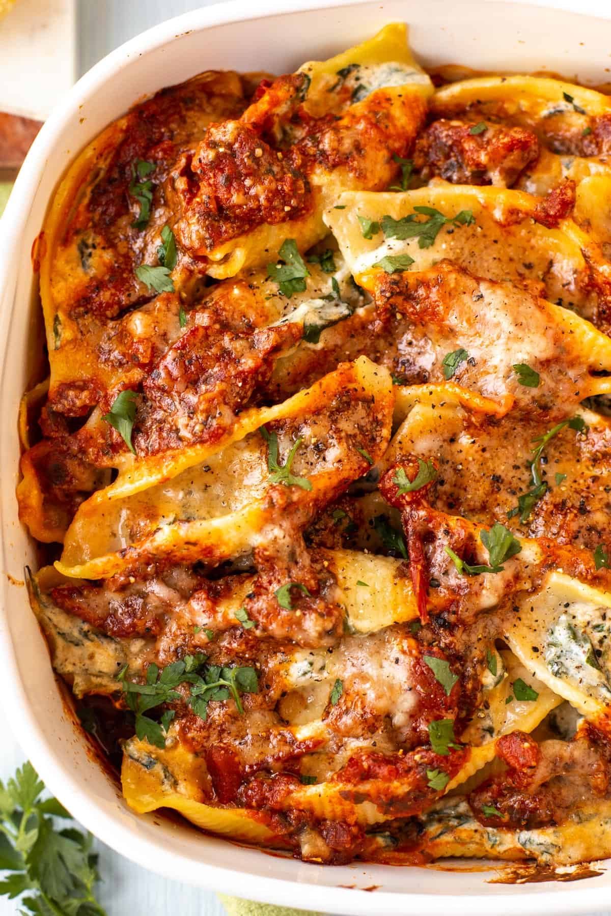 Aerial shot of cheesy stuffed shells in a baking dish, topped with fresh herbs and cheese.