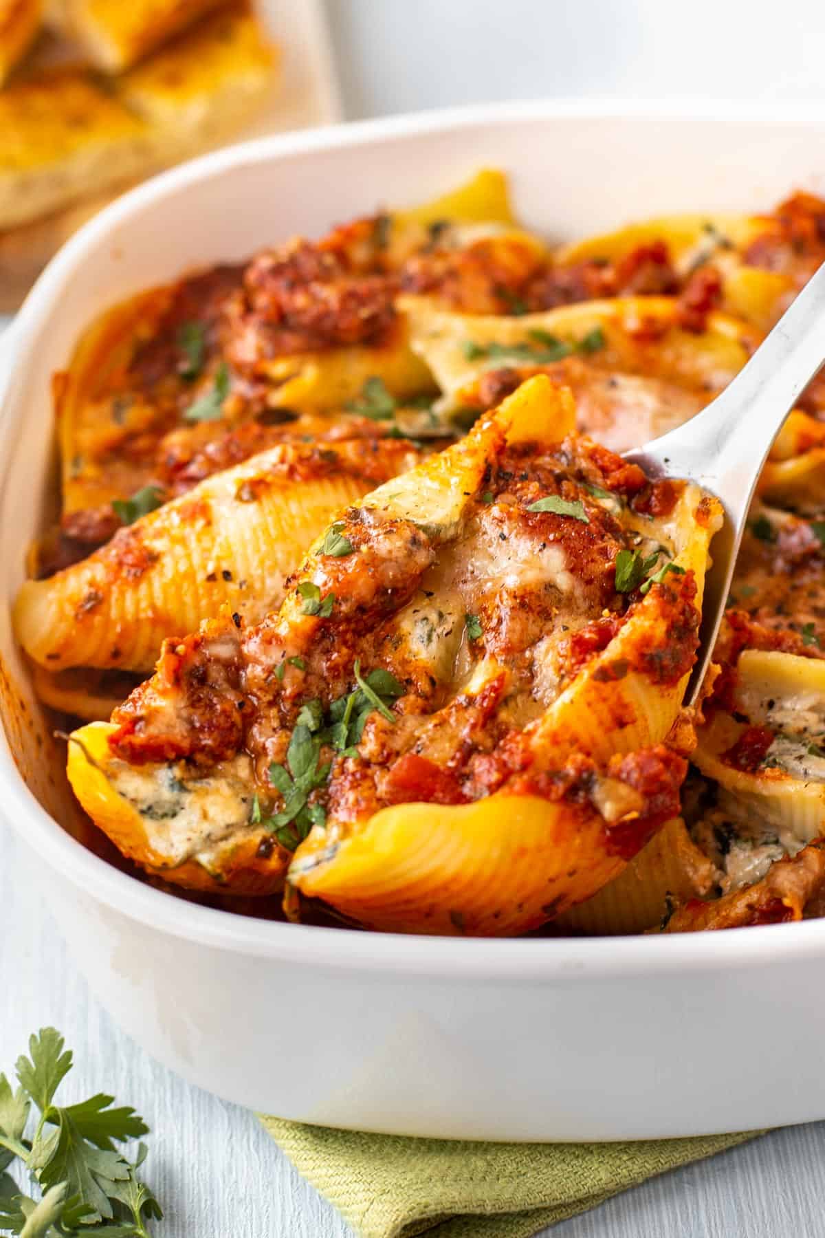 A spoon scooping some spinach and ricotta pasta shells with tomato sauce from a baking dish.