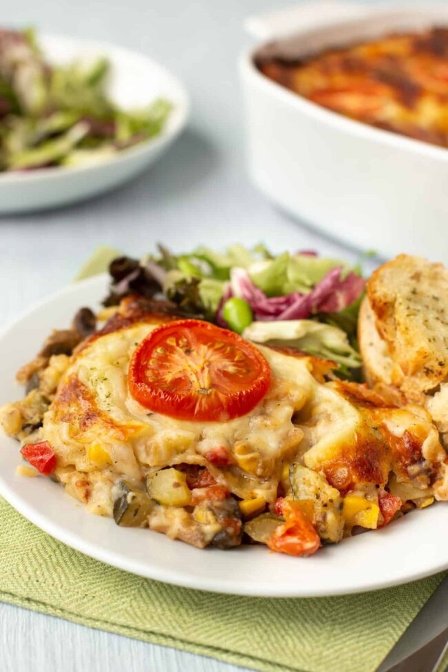 Summer vegetable lasagne A portion of cheesy vegetable lasagne on a plate with salad and garlic bread.