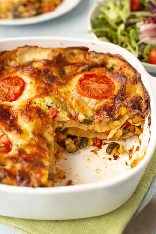 A creamy vegetable lasagne in a dish with a slice removed.