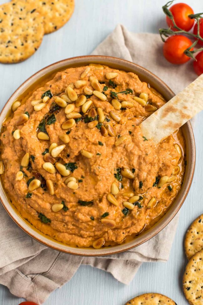 Tomato hummus being scooped with a stick of pitta bread.