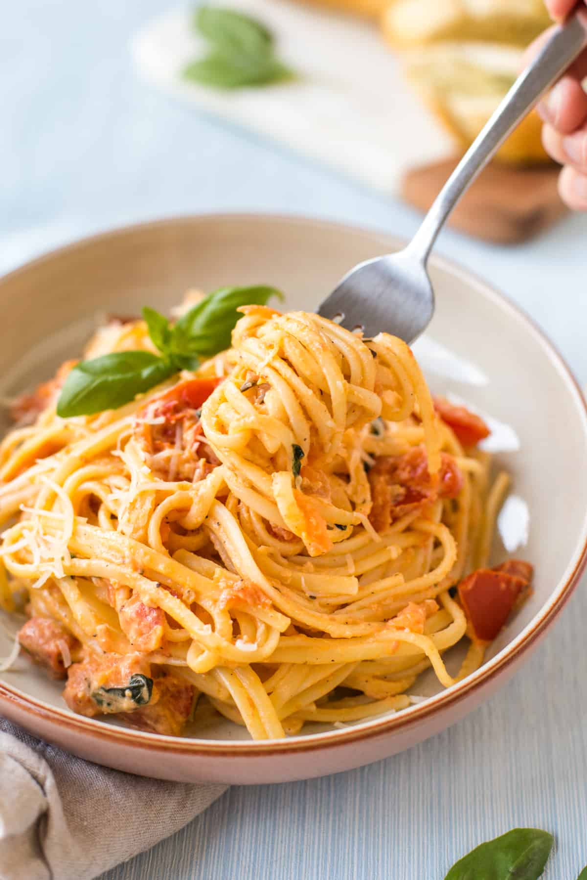 A fork taking a scoop of tomato and mascarpone pasta from a bowl.