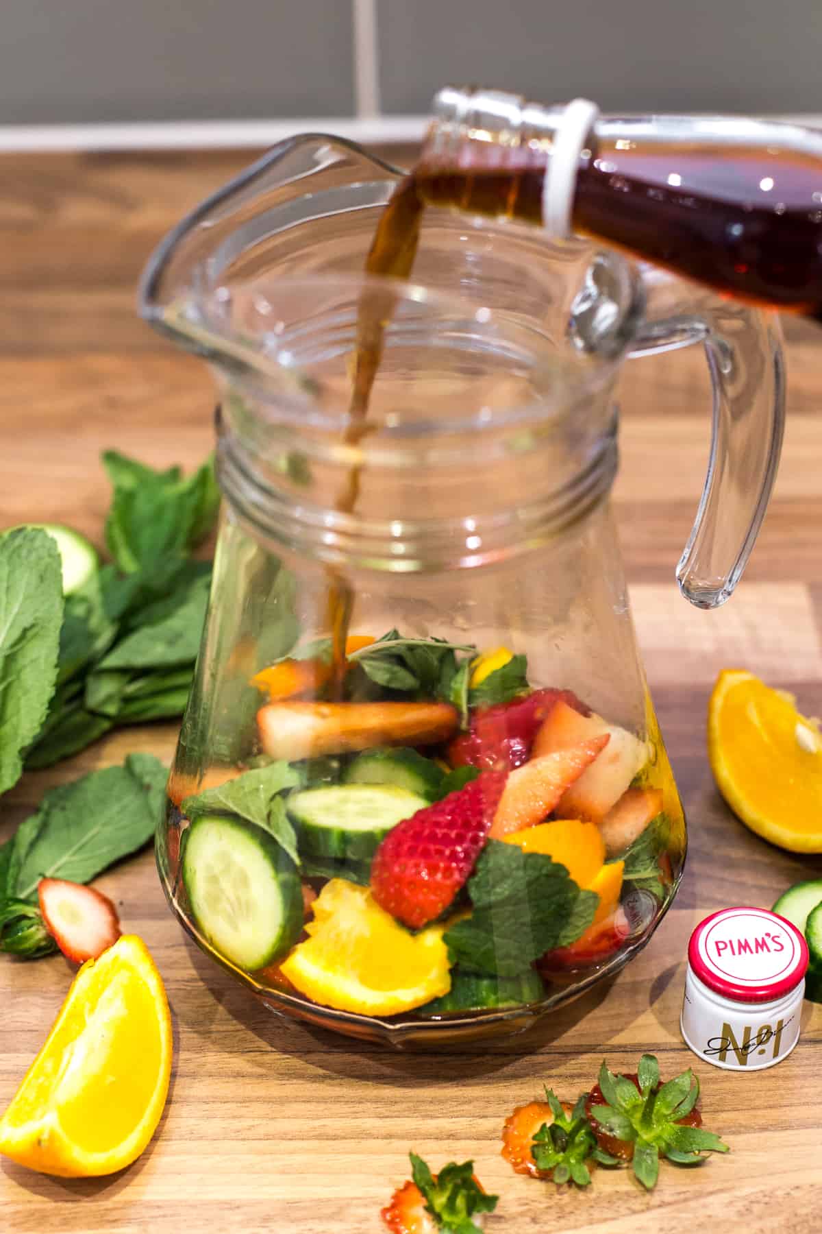 Pimm's being poured over fresh fruit in a glass jug.