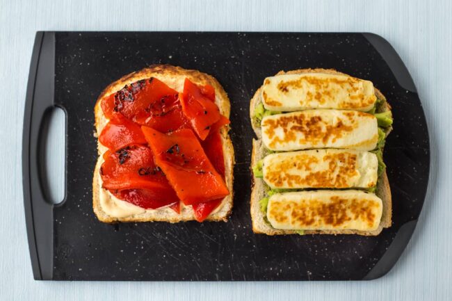 A sandwich being made on a board with fried halloumi and roasted red peppers.
