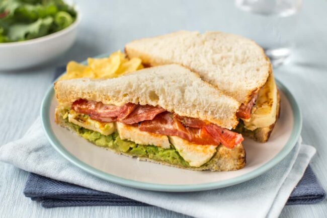 A vegetarian halloumi sandwich cut in half on a plate.