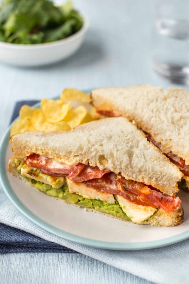 A fried halloumi and roasted red pepper sandwich on a plate, cut in half.