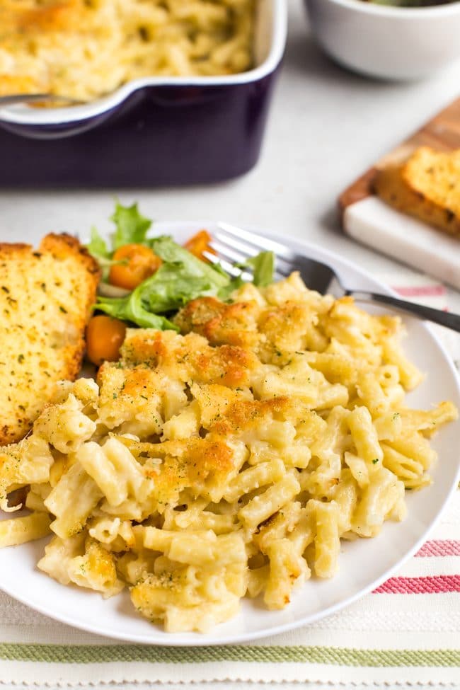 Portion of macaroni cheese on a plate with garlic bread and salad