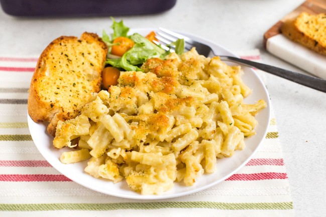 Portion of macaroni cheese on a plate with salad and garlic bread
