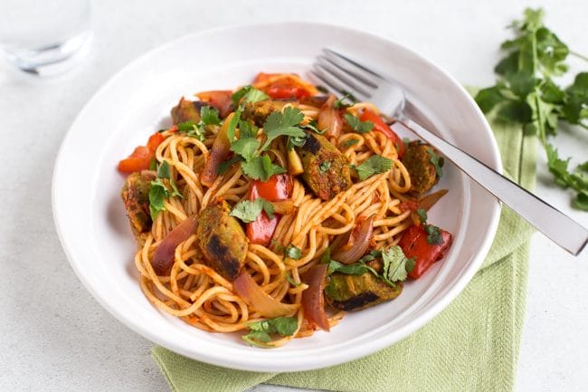 Portion of vegan curried sausage pasta in a bowl topped with cilantro