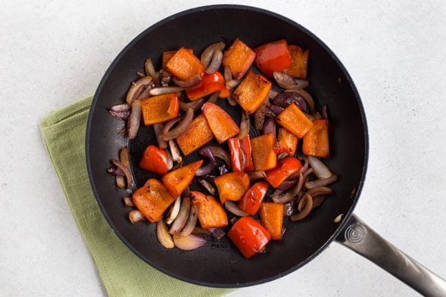 Peppers and onions cooked in a frying pan on a green napkin